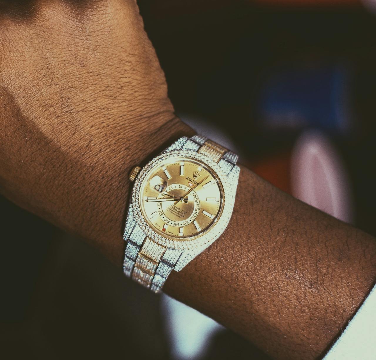 about-01 Close-up of a luxury gold watch with a diamond-studded bezel on a person's wrist.